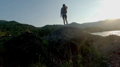 The setting sun illuminates the mountains and the turbulent river. The girl Stock Footage 278365927