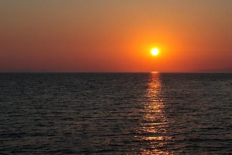 Setting sun over the sea, clear reddish sky Stock Photos