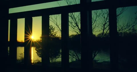 Setting sun over water shot from behind a balcony railing in cottage country Stock Footage 130913044
