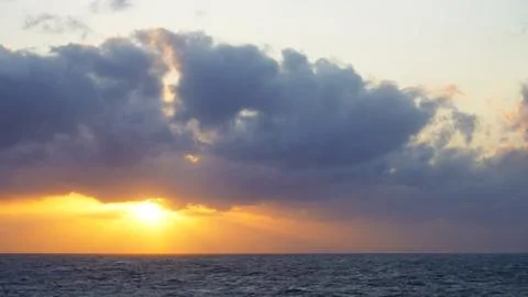 Setting sun peeks from behind of grey stormy clouds Stock Photos