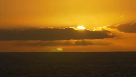 Setting sun peeping through a trail of cloud over the sea Stock Footage 77803832