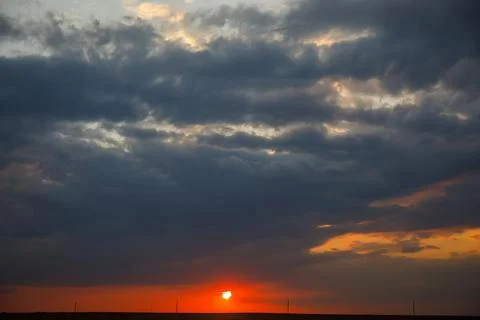 The setting sun in red against a background of blue clouds and a sky of blue, Stock Photos