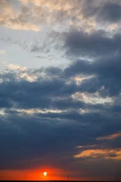 The setting sun in red against a background of blue clouds and a sky of blue, Stock Photos