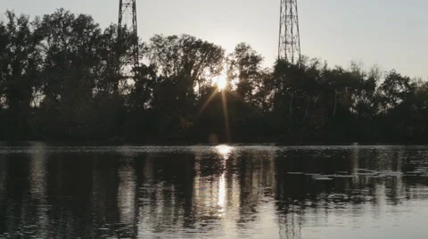 The setting sun shines through the trees on the river bank Stock Footage 55650999