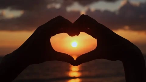 Setting sun shining through heart-shaped hands. Day of Peace concept. Vidéo 248489014
