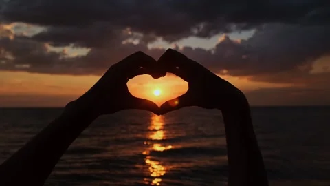 Setting sun shining through heart-shaped hands. Day of Peace concept. Video stock 249229498