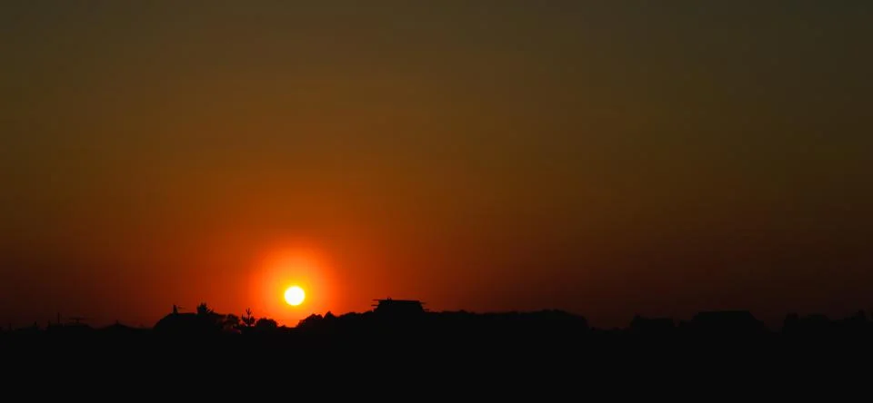 The setting sun at sunset in the orange evening sky above the silhouettes Stock Photos