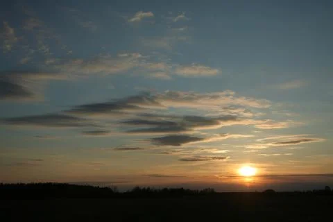The setting sun through the clouds over the field in the silence of the eveni Stock Photos