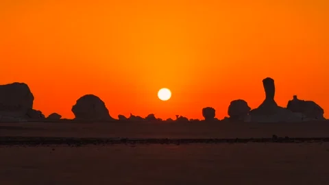 Setting sun touching horizon behind white desert rock formations silhouettes 库存影片 340868333