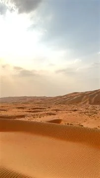 Setting suns rays pierce through soft clouds, lighting up desert dunes with rich Stock Photos