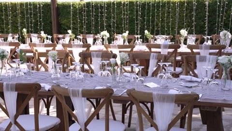 Setting up tables for a wedding under string lights in a garden space Stock Footage 335996012