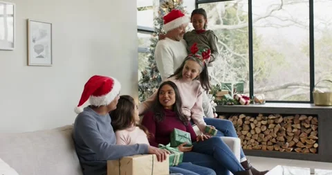 Settling onto sofa by Christmas tree family passing gifts and sharing laughter Stock Footage 335453887