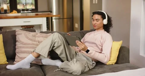 Settling on sofa at home non-binary person grabbing tablet slipping on Stock Footage 337224272
