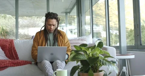 Settling on sofa in living room, man with dreadlocks typing and scrolling on Stock Footage 335866717