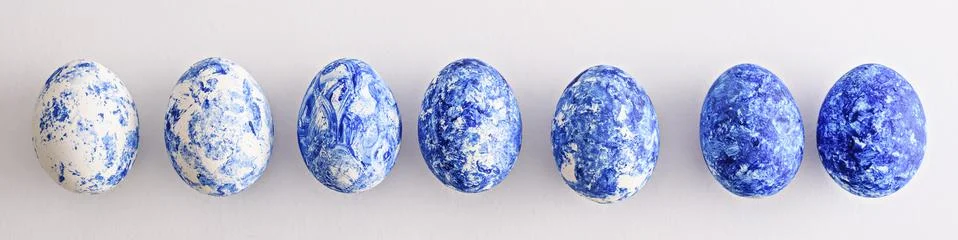 Seven Easter eggs with blue gradient effect in row on white background for ba Stock Photos