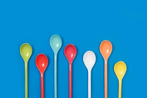 Seven plastic colored spoons on a blue background Stock Photos