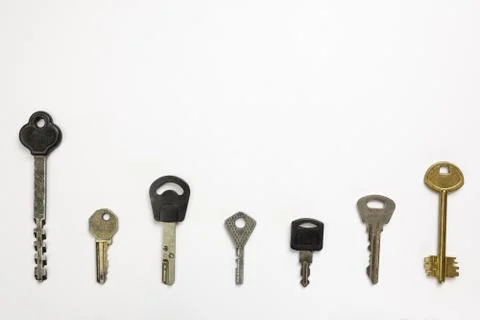 Seven types of different door keys lie in a row on a white background under c Stock Photos
