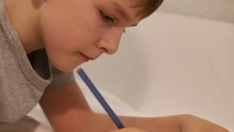 A seven-year-old boy passionately drawing with a simple pencil lying on the couc Stock Footage 170309259