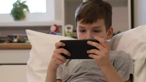 A seven-year-old boy is playing a smartphone on the bed. Stock Footage 170310241