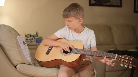 A seven-year-old boy plays the guitar in the room. Video stock 281016454