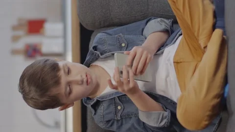 A seven-year-old boy sits on the sofa and plays on the phone. Stock Footage 152045520