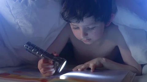 Seven year old caucasian boy enjoying reading interesting fairytale lying in Stock Footage 130001034
