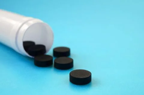 Several black tablets fall out of the plastic jar on the blue surface. Back.. Stock Photos