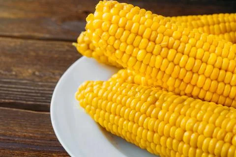 Several boiled heads of corn on a white plate on a wooden table. Close-up. 스톡 사진
