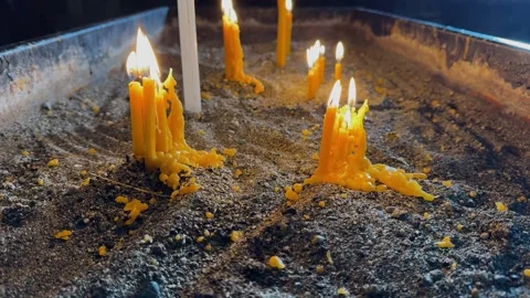 Several burning yellow candles with dripping wax on a sandy surface. Видео 265583035