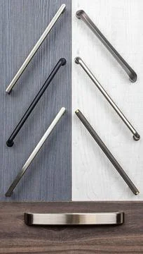 Several cabinet handles lay on a table with two types of wood surfaces. The h Stock Photos