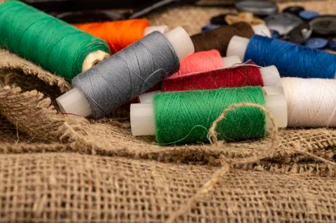 Several coils of multicolored sewing thread against a background of coarse-te Stock Photos