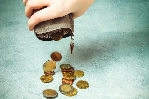 Several coins fall on the table from an empty wallet in a woman's hand, pover 스톡 사진