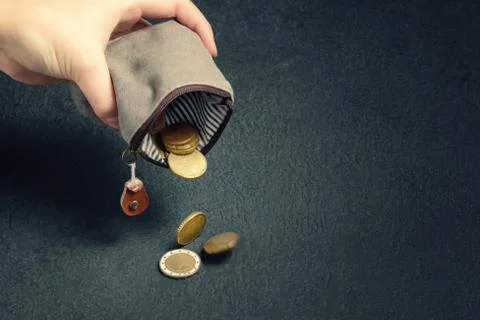 Several coins fall on the table from an empty wallet in a woman's hand, pover Stock Photos
