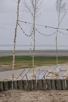 Several colourful deckchairs and tree trunks on the sandy beach, fairy lights Stock Photos