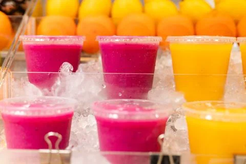Several cups filled with vibrant fruit drinks sit on a layer of ice. Bright.. Stock Photos