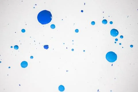 Several drops and splashes of blue ink spread across a white paper. Stock Photos