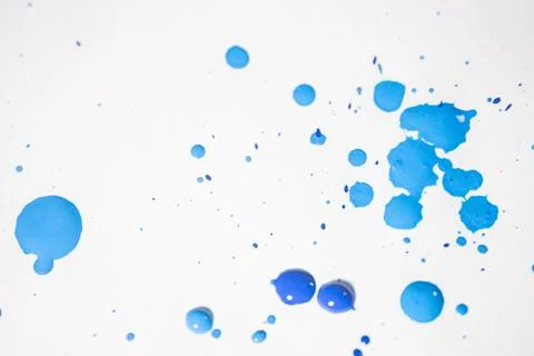 Several drops and splashes of blue ink spread across a white paper. Stock Photos