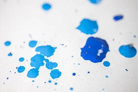Several drops and splashes of blue ink spread across a white paper. Stock Photos