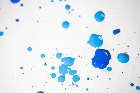 Several drops and splashes of blue ink spread across a white paper. Stock Photos