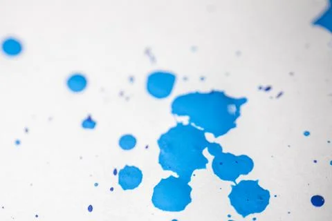 Several drops and splashes of blue ink spread across a white paper. Stock Photos