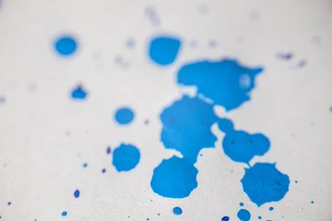 Several drops and splashes of blue ink spread across a white paper. Stock Photos