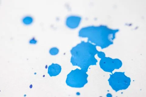 Several drops and splashes of blue ink spread across a white paper. Stock Photos