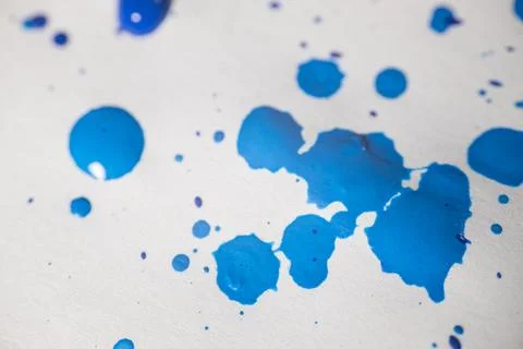 Several drops and splashes of blue ink spread across a white paper. Stock Photos