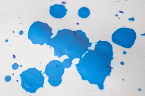 Several drops and splashes of blue ink spread across a white paper. Stock Photos