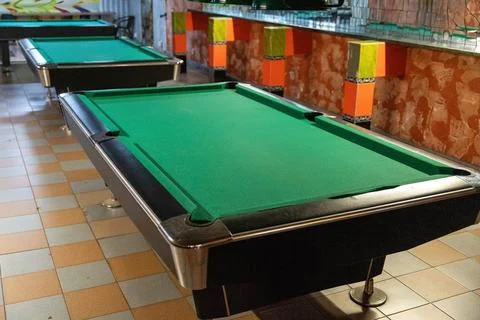Several empty pool tables with bright colored decor in the background Stock Photos