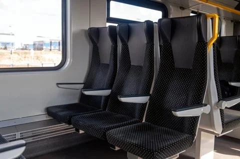 Several empty train seats are aligned in a clean train interior near a window Stock Photos