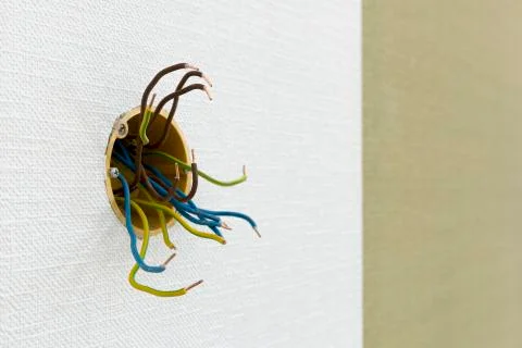Several exposed electrical copper wires protruding from a whitewall. Stock Photos