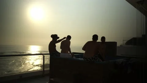 Several friends sitting at the edge of a pool in a house overlooking the beach Video stock 181909651