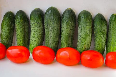 Several green cucumbers and red tomatoes are stay in a rows on a white backgr Stock Photos