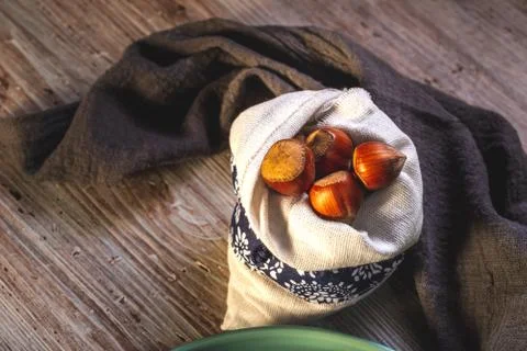 Several hazelnuts in white bag placed on wooden board Stock Photos